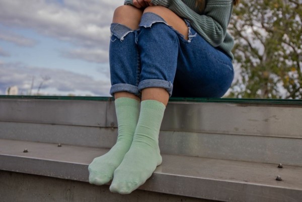 A person wearing jeans and bamboo socks, sitting on a fence
